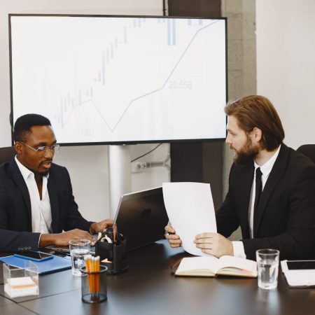 African man in a black suit. International partners. People sitting at the table with laptop.